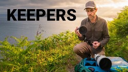Wildlife photographer holding telephoto lens with camera bag and blue equipment case by coastal landscape