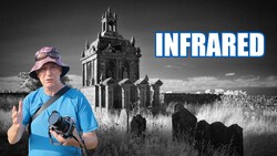 Photographer holding infrared camera in front of gothic tower ruin, wearing blue shirt and pink hat