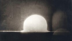 Nuclear explosion test shot showing bright hemispherical fireball rising above desert ground with shock wave and dust plume
