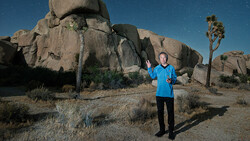 Runner in blue shirt posing in front of large granite boulders under starry night sky