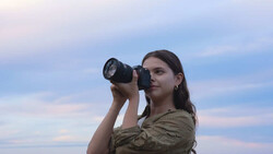 Female photographer holding DSLR camera to eye while composing shot against twilight sky