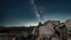 Milky Way galaxy rising above desert landscape with illuminated memorial plaque on boulder