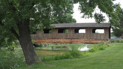 Wooden boathouse with arched openings spanning a calm pond, framed by mature trees