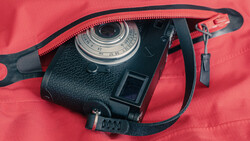 Vintage rangefinder camera with red camera strap on coral fabric background
