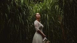 Woman in lace top and flowing skirt standing in tall green corn stalks, looking upward