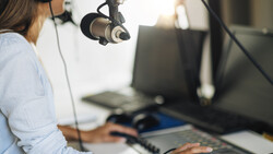 Podcaster recording into a large-diaphragm condenser microphone at a desktop studio setup