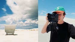 Photographer holding camera in desert landscape beside minimalist white structure
