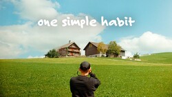 Person photographing rural farmhouses across an open green field under blue sky with text overlay