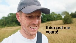 Man in baseball cap smiling at camera with rural field and trees in background