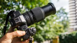 Hand holding a DSLR camera with telephoto lens outdoors in daylight