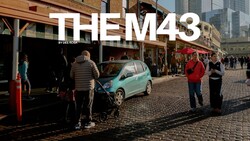 Turquoise compact car parked on cobblestone street with pedestrians and storefronts