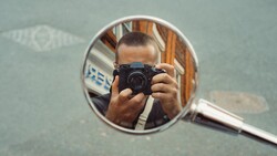 Photographer holding compact camera reflected in round mirror during self-portrait