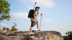 Hiker with backpack and trekking pole standing on rocky terrain against blue sky