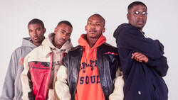 Four men in casual streetwear posed together against a neutral background