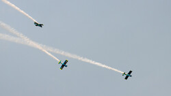 Three aerobatic aircraft in formation flight with smoke trails against a clear sky