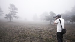 Photographer in white shirt shooting in dense fog among scattered trees