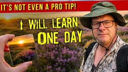 Photographer in wide-brimmed hat and glasses holding smartphone displaying landscape sunset photo