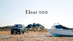 Blue Land Rover parked on sandy beach next to moored fishing boat and rocky outcrop