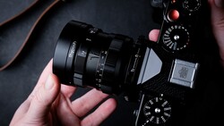 Hands holding a vintage rangefinder camera with attached lens, viewed from above