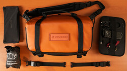 Orange Wandrd camera bag with black straps displayed flat with accessories on orange background