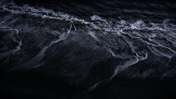 Aerial view of dark ocean water with white wave patterns and foam trails