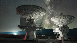 Two large radio telescope dishes under the Milky Way at night with moonrise on the horizon