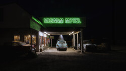 Wigwam Motel storefront at night with neon green sign and parked vintage car