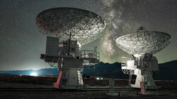 Two large radio telescope dishes pointing skyward beneath the Milky Way at night