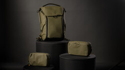 Tan and black camera backpack and modular pouches displayed on black cylindrical pedestals