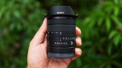 Sony FE 35mm f/1.4 G lens held in hand against blurred green foliage