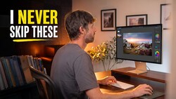 Photographer reviewing landscape image on monitor at desk with warm ambient lighting