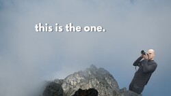 Photographer with telephoto lens photographing a dramatic rocky mountain peak shrouded in mist
