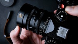 Hands holding a cinema camera lens with focal length markings visible on dark background