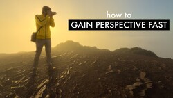 Photographer in yellow jacket standing on rocky terrain at sunrise with mountains in background