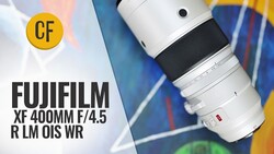 Fujifilm XF 400mm F/4.5 R LM OIS WR telephoto lens with white barrel and black grip ring, shown on a colorful abstract painted background