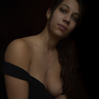 Woman with long dark hair wearing an off-shoulder black top against a dark background