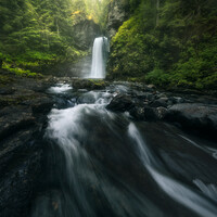 Waterfall cascading into a river with long exposure motion blur effect surrounded by dense green forest