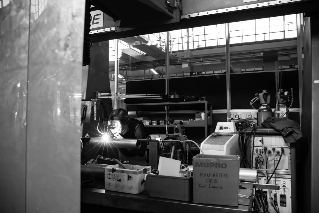 A welder checks the work done by a welding robot at CERN - Photo by Mask Mae
