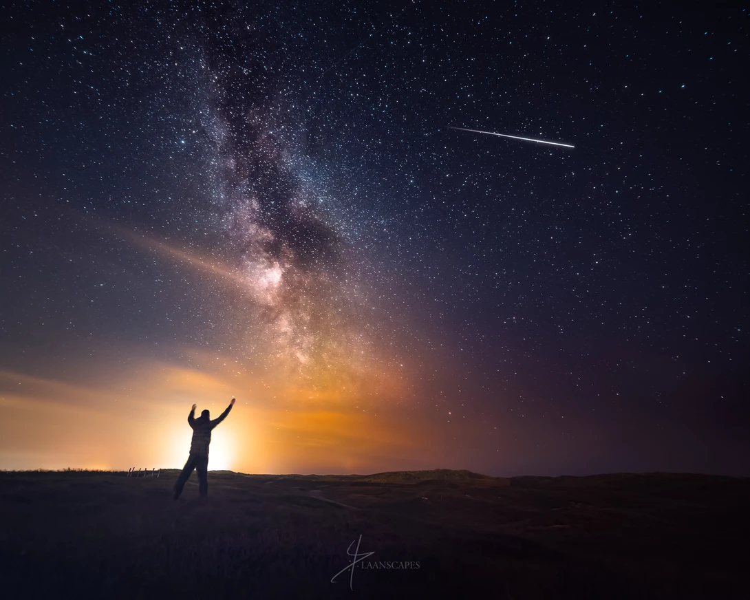 Photograph of a man greeting the International Space Station with the Milky Way overhead.