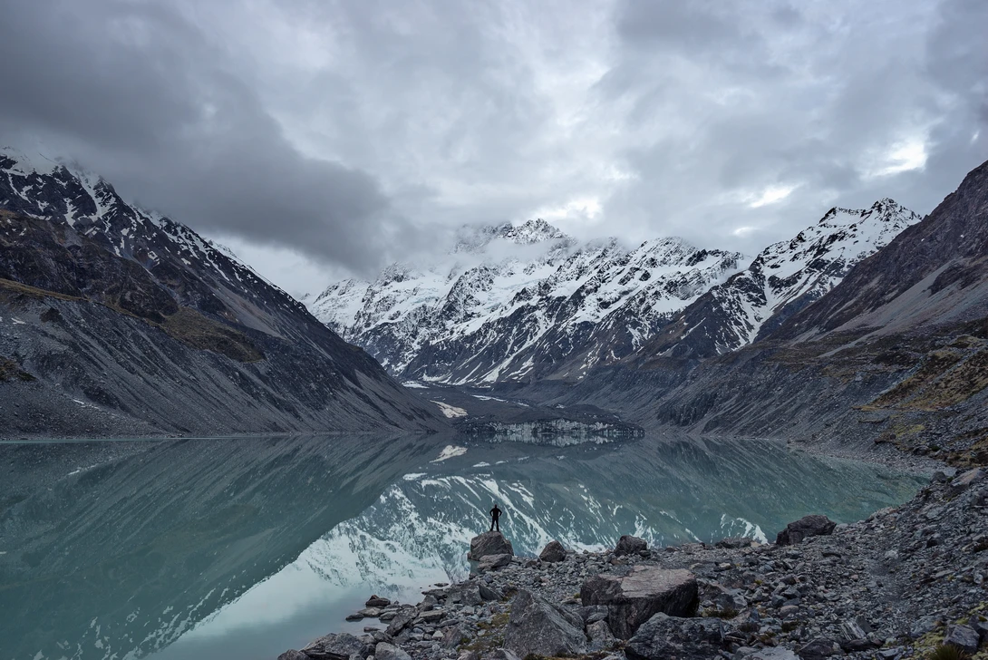 Person at a lake in a vast mountain landscape.