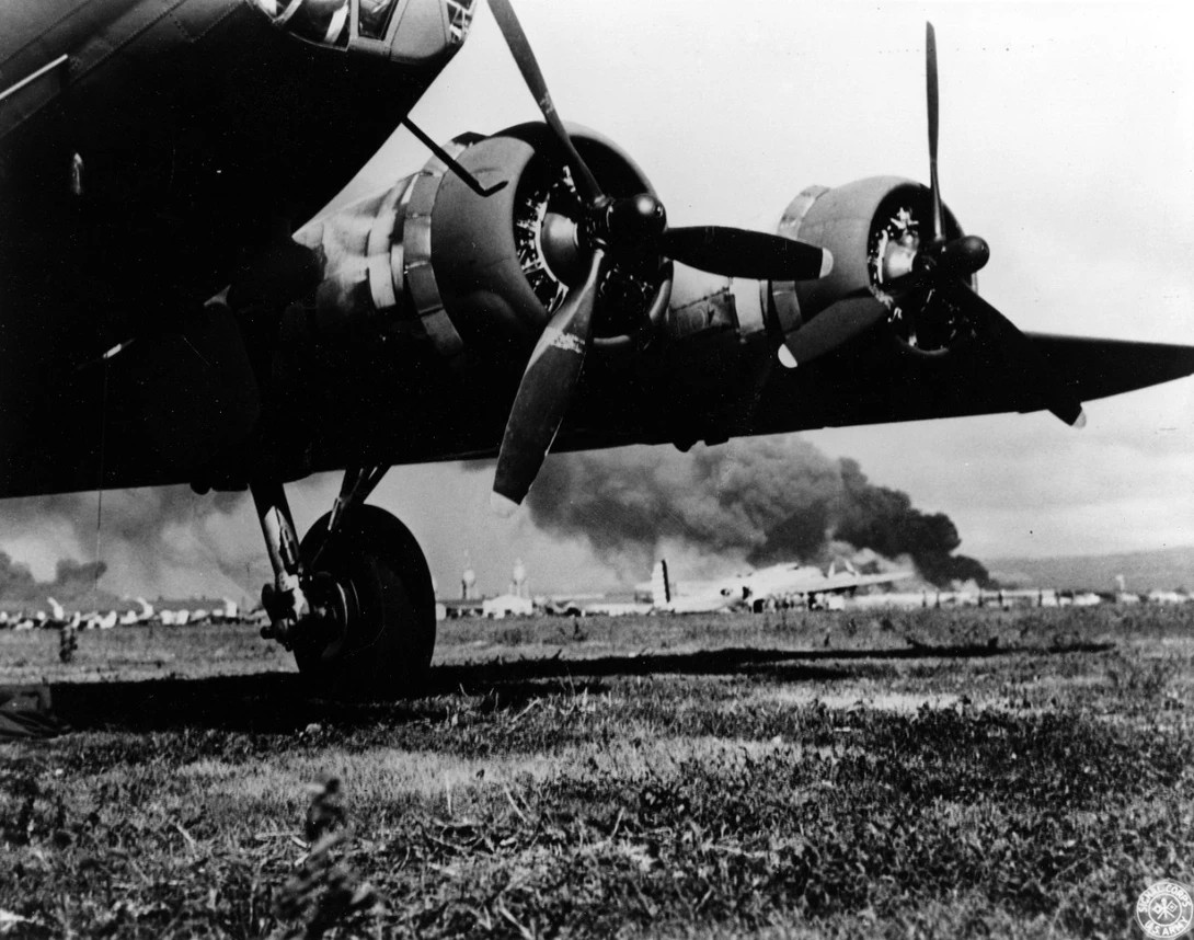 "A U.S. Army B-17E at Hickam Air Field, after landing safely during the Japanese air raid. Smoke from burning ships at Pearl Harbor is visible in the distance. Photographer may be Staff Sergeant Lee Embree."