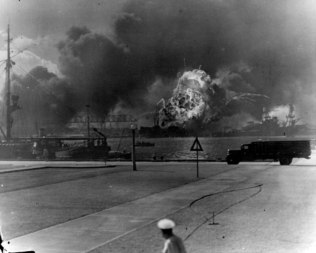 Explosion of the forward magazines of USS Shaw in the floating drydock, after a bombing attack by Japanese planes on 7 December 1941. USS Nevada, also hit by the attackers, is at right. Photographed from Ford Island, with USS Avocet partially visible at 