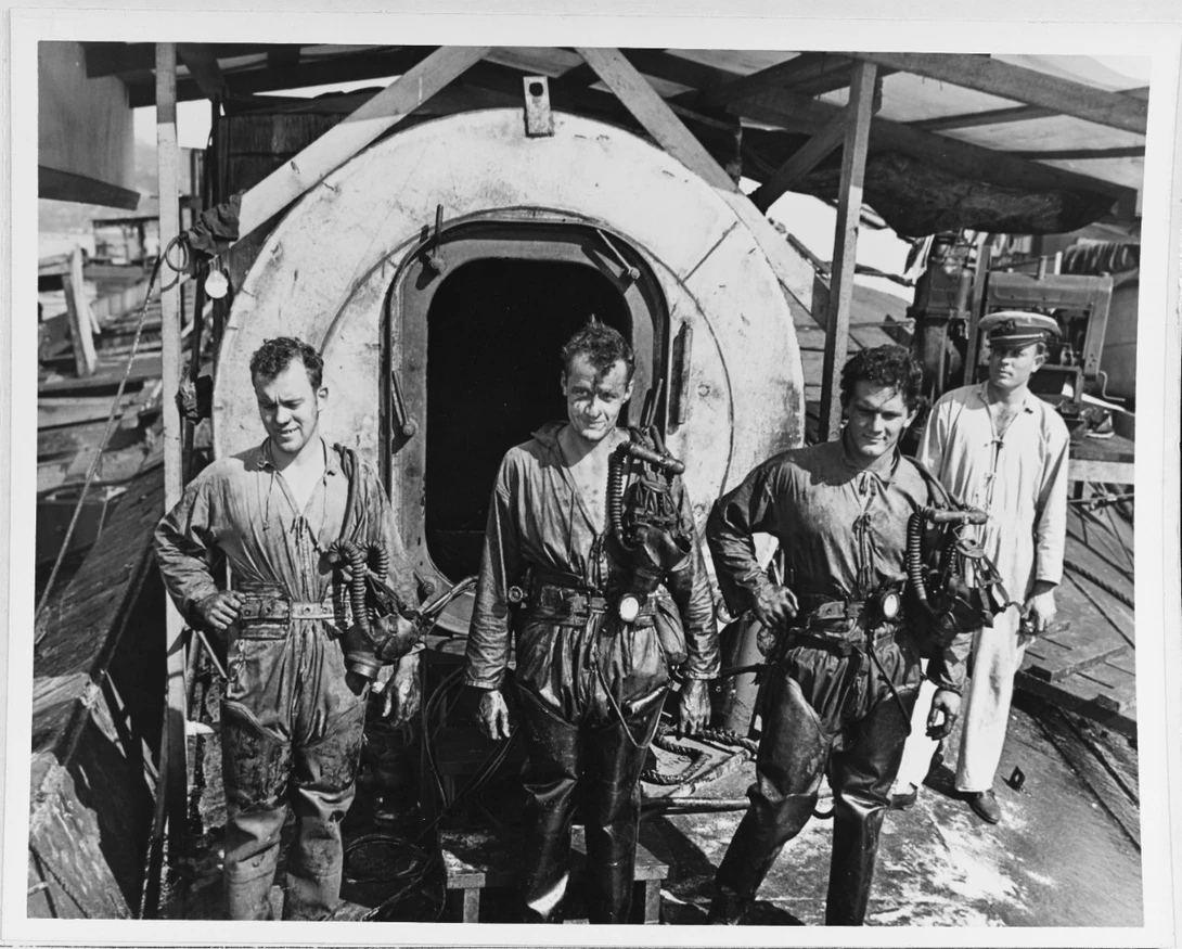 Taking the time to pose during cleanup. "Divers standing in front of a decompression chamber, while they were working to salvage ships sunk in the 7 December 1941 Japanese air raid on Pearl Harbor. Note warrant officer standing at right."