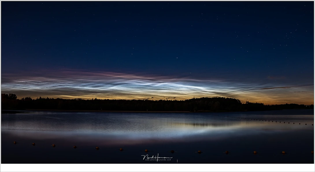 A clear panoramic view at a nearby swimming lake. Twilight colors show at the bottom, and the red glow of the noctilucent clouds appears at the top. Stars are visible through the clouds and in the night sky. (Lumix DC-S1 + 49mm | ISO1600 | f/5,6 | 4 sec)