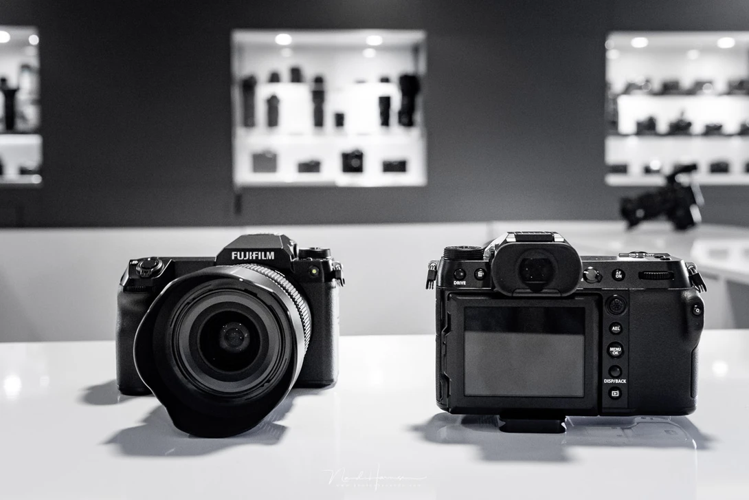Two Fujifilm mirrorless cameras displayed front and rear view on white surface.