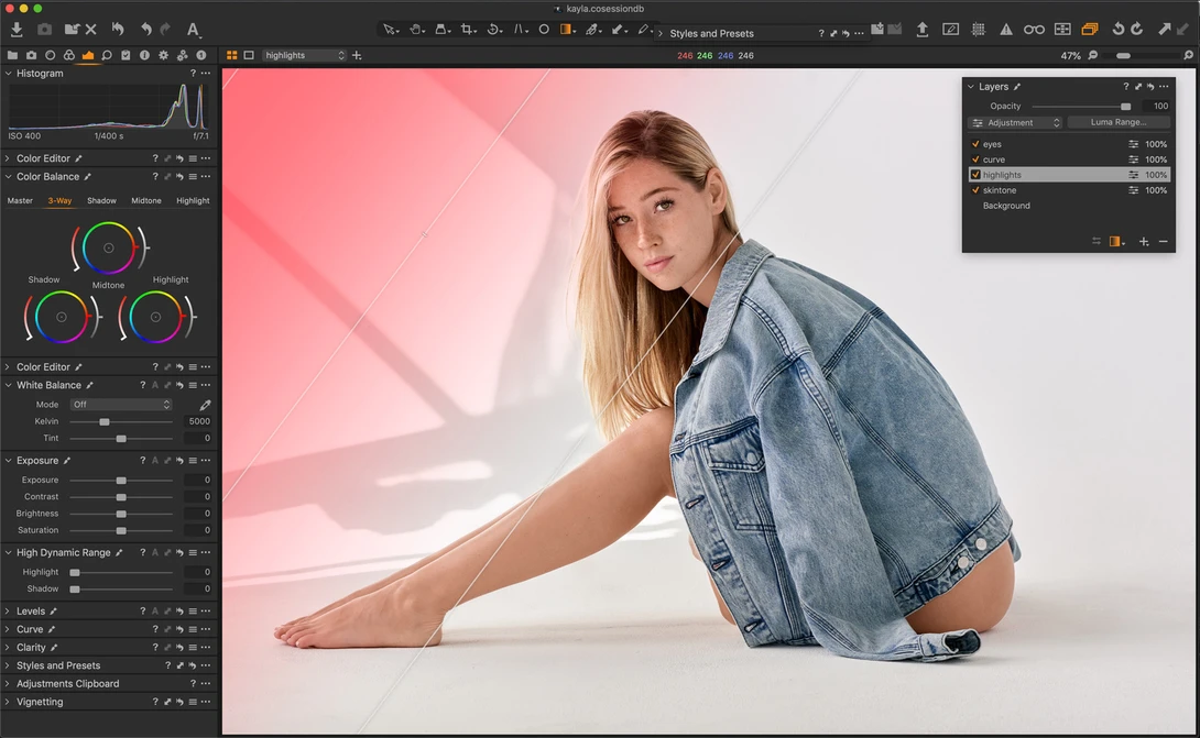 Woman in denim shirt posing against pink and white geometric background in studio setting.