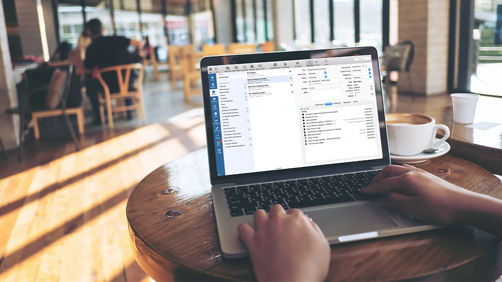 Photographer's hands at laptop displaying file management interface in bright cafe setting.