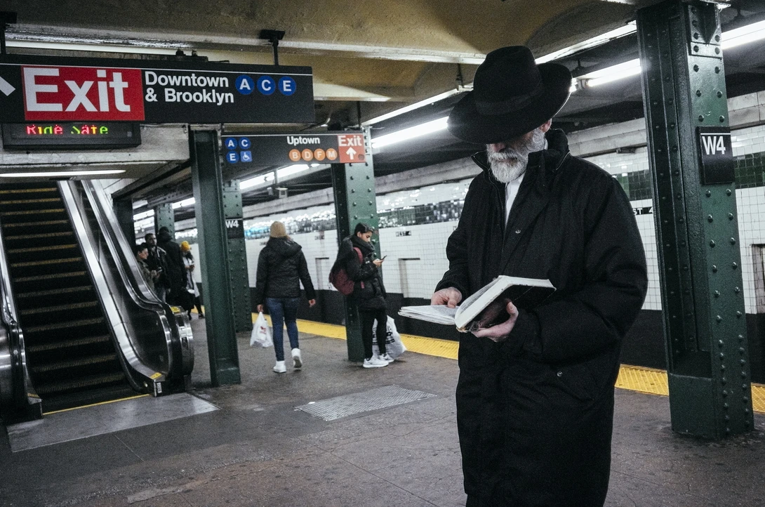 Candid portrait of a man reading a book on a subway platform.