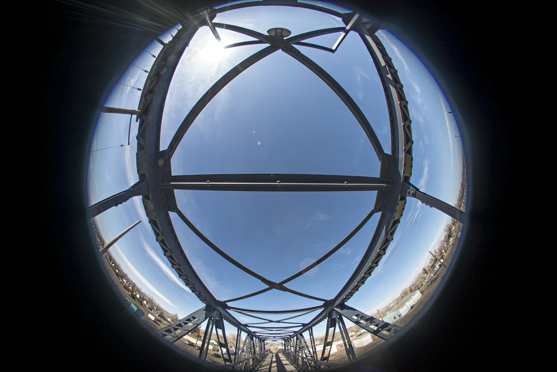View through a circular metal framework looking up at sky and architectural structure below.