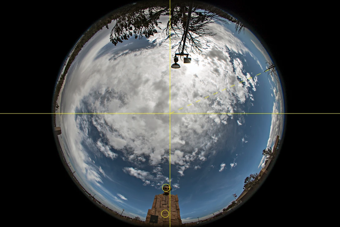 Fisheye view of Earth from space with satellite solar panels and antenna in foreground.